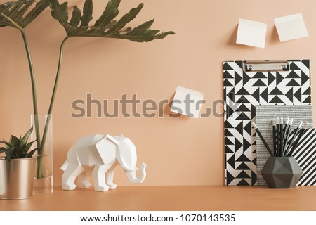 Pastel orange desk with leafs, elephant, plant, office accessories and sticky notes. Artist workspace.