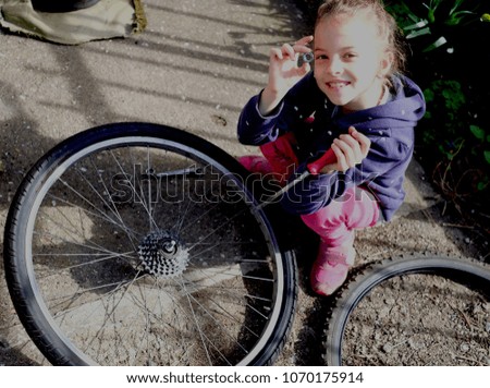 Cute little girl smiling and looking at camera while repairing a bicycle