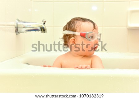 Baby girl plays in a bathtub wearing swimming goggles.