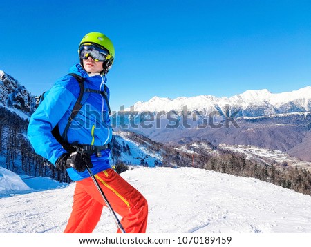 Photo of skier wearing helmet against background of mountains and blue sky