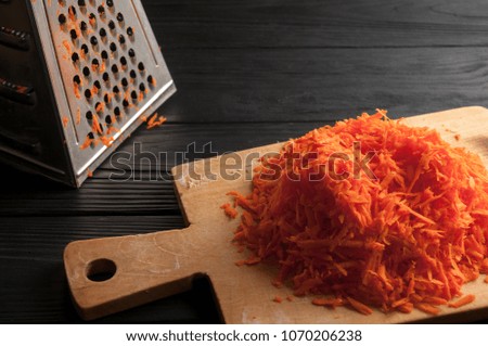 Grated carrots on a blackboard against a wooden background with a metal float