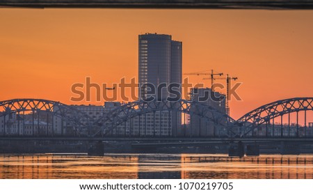 Panoramic view of Riga city in colorful evening sunset. Iconic bridge, promenade, skyscrapers and river Daugava. Atmospheric scenery in urban territory. 
