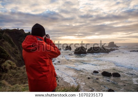 Man with a camera is looking at a Beautiful Pacific Ocean Coast with rugged rocky formation in the background. Taken in Ecola State Park, Seaside, Cannon Beach, Oregon, USA.