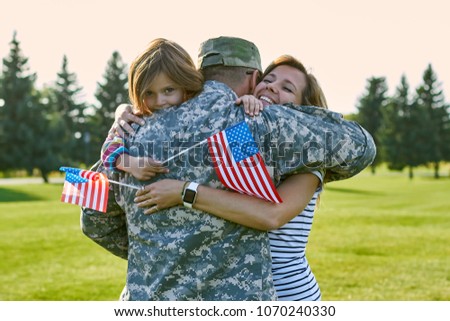 Happy soldier with his family in the sunny day. Close up hugs, reunion in the park lawn.