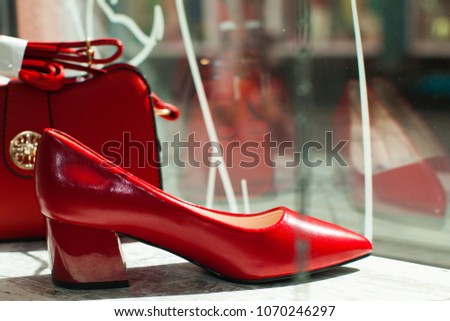 Red leather shoes near a glossy black bag, dramatic lighting. Beautiful woman bag lying on wooden floor near red feathers.
