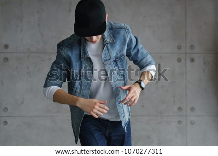 Teenage guy wearing denim jacket and white sweater is dancing hip-hop with baseball cap. Dynamics and plastic movement of modern dance.