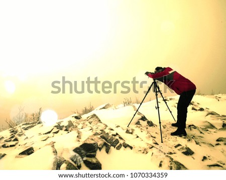 Abstract effect.  Travel photographer doing pictures in ancient stones on snowy peak of mountain. Winter cold and misty morning in mountains
