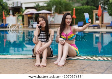 two young women friends using mobile phone in the swimming pool
