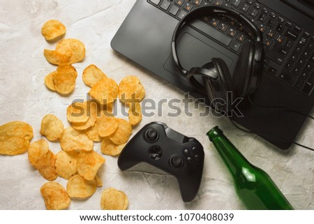 Laptop, Gamepad, Headphones, Potato chips, Bottle of Beer on a light stone background. Concept of computer games and leisure.