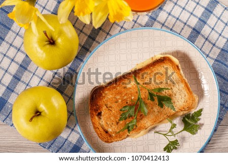Good and delicious food and beverages for breakfast. Toast with butter and cheese, two apples, bouquet of yellow daffodils and glass of orange juice on kitchen napkin. Top view