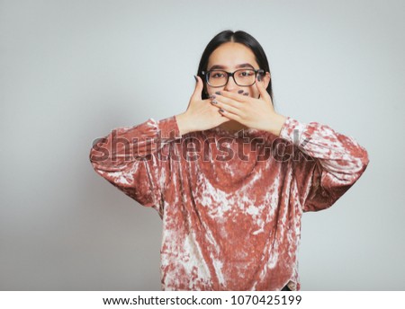 beautiful asian woman hiding her mouth with her hands, wearing glasses and a pink sweater, studio photo on the background