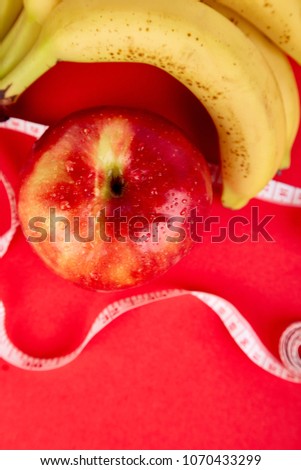 Measuring tape wrapped around a red apple and banana as a symbol of diet on red paper background. Weight loss concept. Diet. Dieting concept. Vegan. Clear food. Healthy. Top view. Minimalism