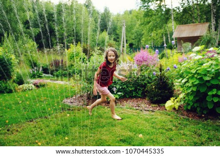 Kid girl playing with garden sprinkler in hot summer day. Water outdoor activities for children, happy childhood.