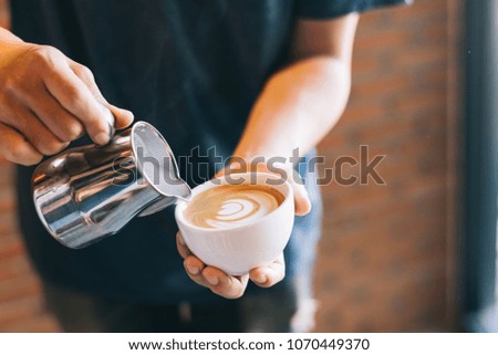 Closeup of male barista holding milk for prepare cup of coffee, latte art.