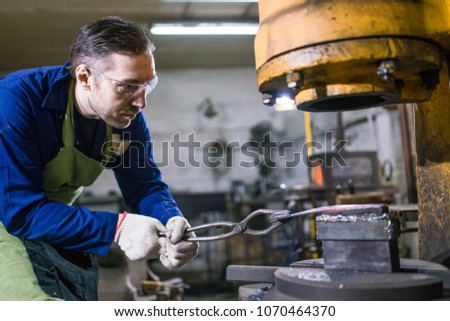 A brutal man works in a workshop, forges iron.