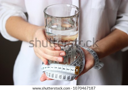 
a glass of water and a centimeter tape in female hands on a light background. use of water. slimming, minimalism, health, diet, proper nutrition.