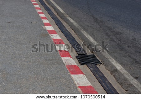 Footpath road. Red and white concrete sidewalk . View of Circuit. racetrack with white lines. White and red striped Parking Sign on Footpath road.