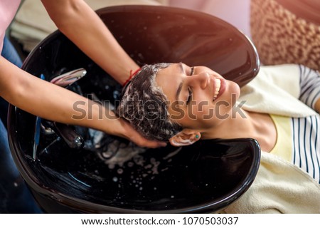 Happy young woman at hair salon washing hair Royalty-Free Stock Photo #1070503037