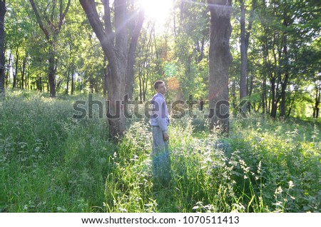 A young guy in a gray sports suit stands opposite the sun among the trees in the forest. Recreation during a sports run in the open air forest. The rapture of a beautiful dawn