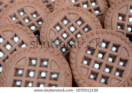 Detailed picture of dark brown round sandwich cookies with coconut filling close up. Background image of several treats for tea