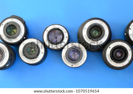 Several photographic lenses lie on a bright blue background. Space for text