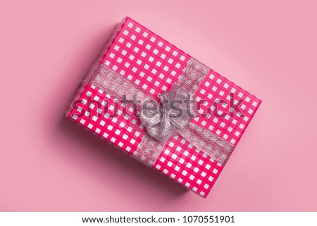 Gift box with a silver bow on a pink background. A checkered gift box. Silvery, brilliant gift bow. Box in the cage. A gift for loved ones. Pink background.