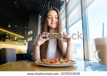 beautiful woman is making photo of food in cafe, latte on table pizza, communication in social networks