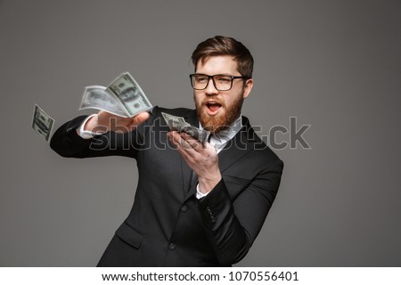 Portrait of a happy young businessman throwing out money banknotes isolated over gray background Royalty-Free Stock Photo #1070556401