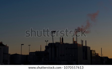 A silhouetted view of a factory and it's smokestacks at dusk