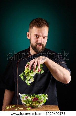 Portrait of a handsome male chef cook making tasty salad on a blurred aquamarine background