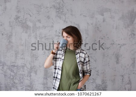 Portrait of charming female student with coffee in casual clothes on gray vintage wall background. looks happily directly into window.Copy space