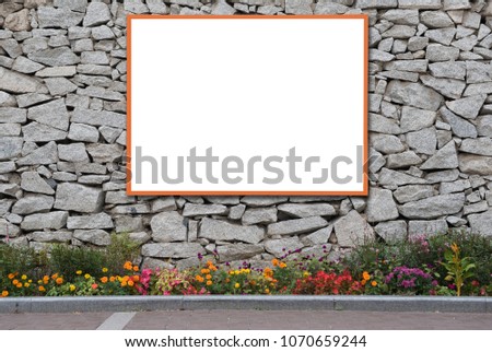 Blank advertising billboard on buildings exterior stone wall or old stone fence with colorful flower bed in spring season on sidewalk or walking street in the city.