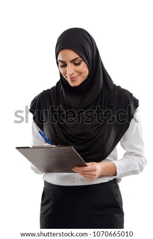 Office worker writing on papers, holding a clipboard. Woman smiles and enjoys her job. Studio portrait, isolated on white.