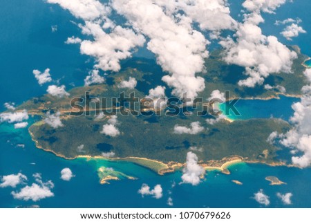 Aerial view of green tropical island in ocean through clouds. Vacation holidays background.  Concept of beach exotic vacation, escape from big city.