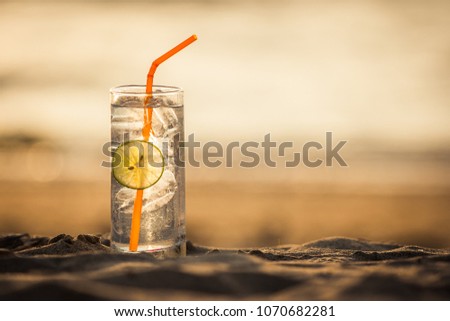 Picture of a glass of Gin Tonic with straw and lime slice on the beach, at sunset. Long Beach, Ko Lanta, Thailand.