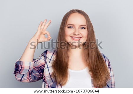 Portrait of pretty attractive cheerful positive model in checkered shirt with long blonde hair gesturing ok sign with fingers looking at camera isolated on grey background, advertisement concept