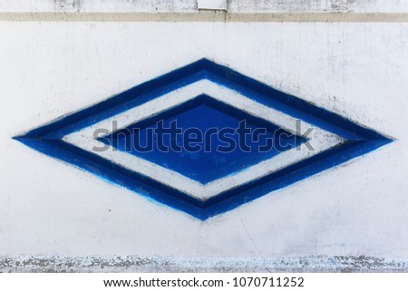 Empty background of a cement stone wall with notches of geometric shape. Abstract web banner. Texture of the rock fence facade with a blue rhombus in the middle.