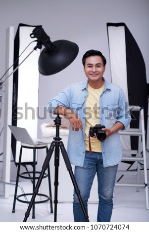 Portrait of cheerful Vietnamese photographer with digital camera in his studio