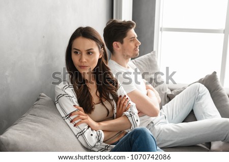 Photo of resentful guy and girl acting like arguing couple and not speaking to each other, while sitting together on couch at home isolated over white background Royalty-Free Stock Photo #1070742086