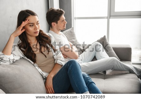 Photo of resentful guy and girl sitting together on couch at home with upset look without conversation isolated over white background Royalty-Free Stock Photo #1070742089
