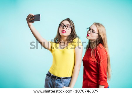 Two beautiful women take a selfie on a blue background.