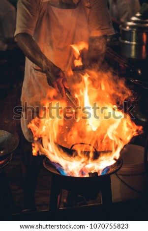 Night picture of a street food chef cooking meat and fish in a pan with fire and flames under it. Chinatown, Bangkok, Thailand