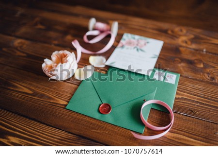 White invitation letter for wedding decorated with flowers and green envelope lie on the table with ribbons