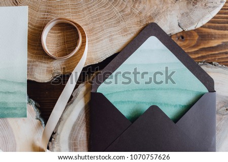 Green invitation letter for wedding decorated with sea waves and violet envelope lie on the table with wooden blocks