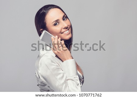 Portrait of a Smiling Young Woman dressed in White Shirt talking on smartphone isolated over neutral background