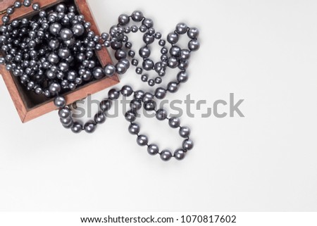 Black pearl necklace in wooden box on white background. Romance, beauty concept. Copy space, top view, flat lay, card layout