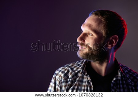 Profile closeup portrait of bearded man looking to the side over dark background, red and blue backlit