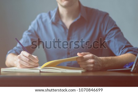 Close up of the hands of a businessman in a blue shirt signing or writing a document on a sheet of notebook. businessman or student writes information from portable prepare for lectures, Vintage color