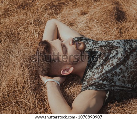 Portrait of a young guy with a beard resting in the field on a sunny day in the spring
