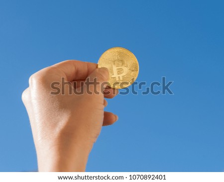 Hand holding golden bitcoin coin on blue sky background
